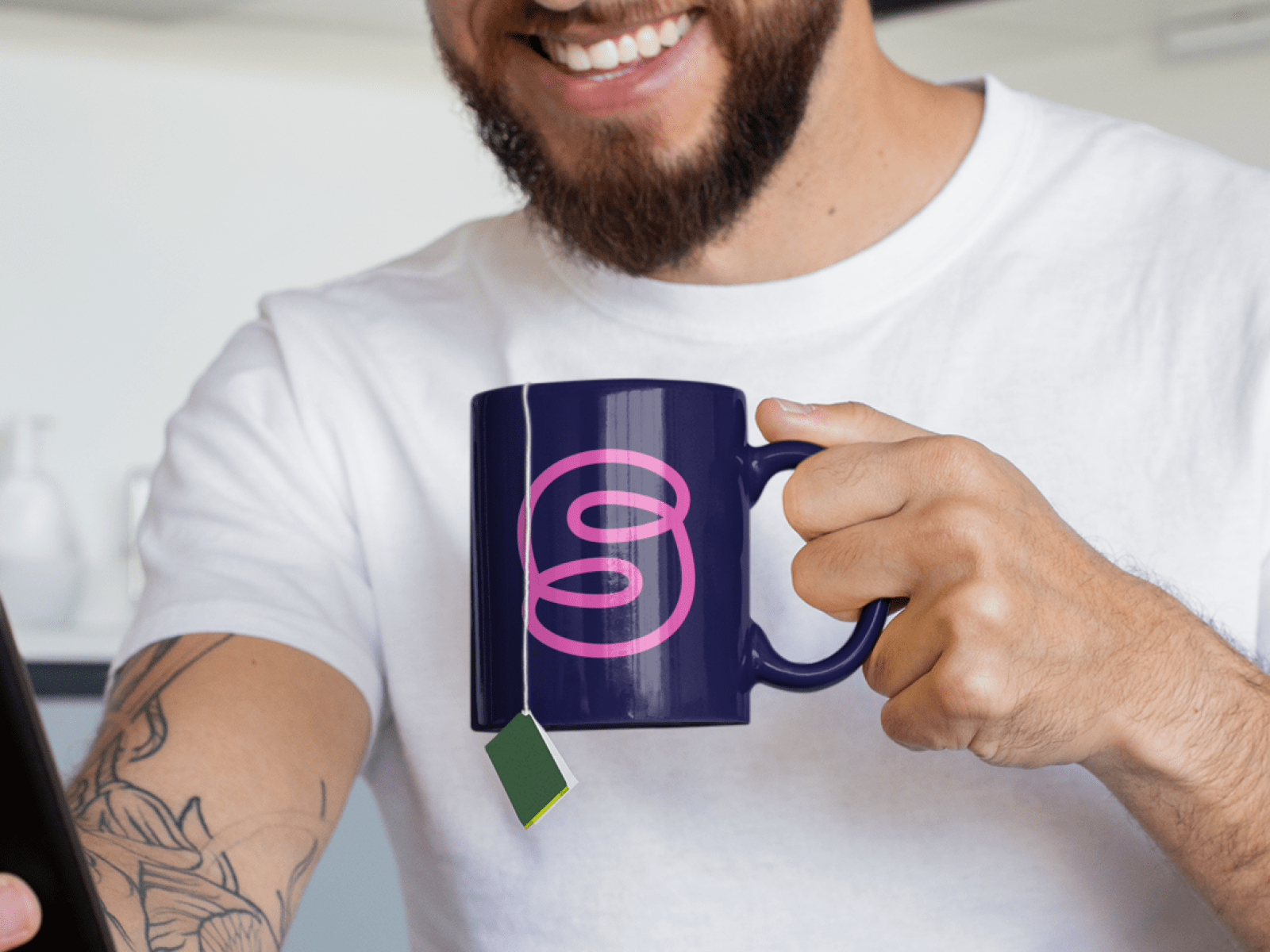 Mann, der eine dunkelblaue Tasse mit dem good space. Logo darauf hält und ein Smartphone in der anderen Hand.